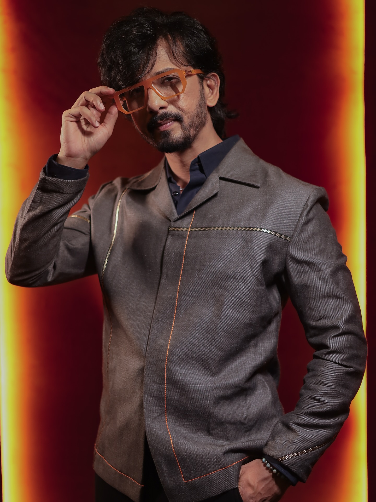 Actor stuns in elevated style with statement glasses and edgy outfit under dramatic lights.